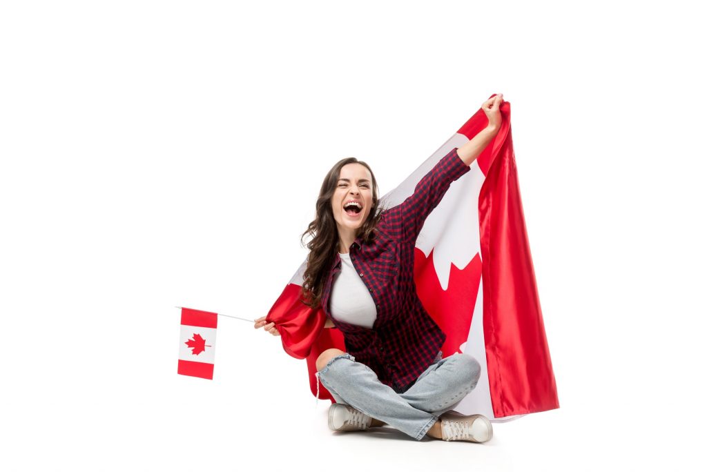 excited woman covered in canadian flag holding maple leaf flag isolated on white